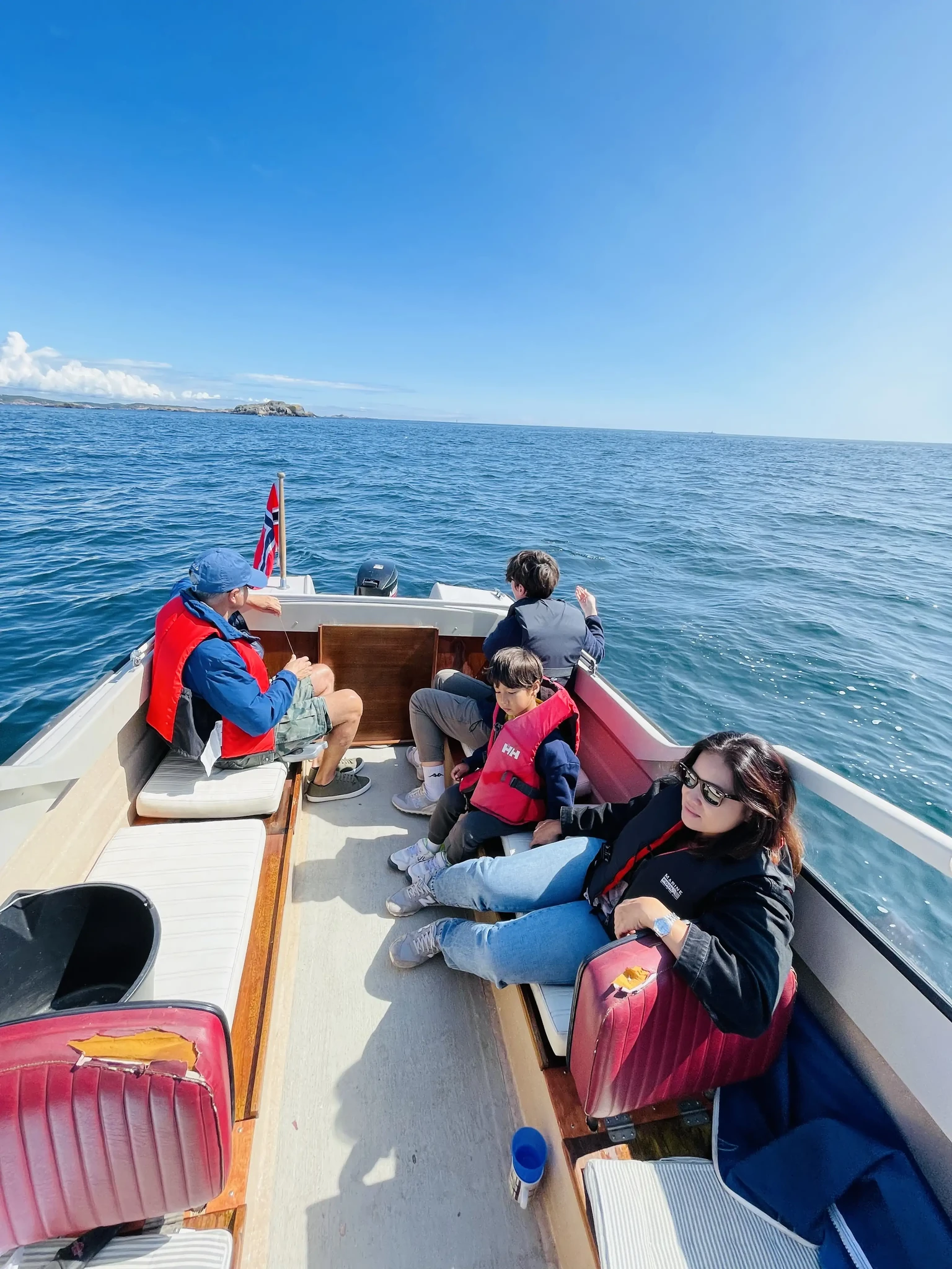 Four people sitting in an open boat at sea beneath a blue summer sky.