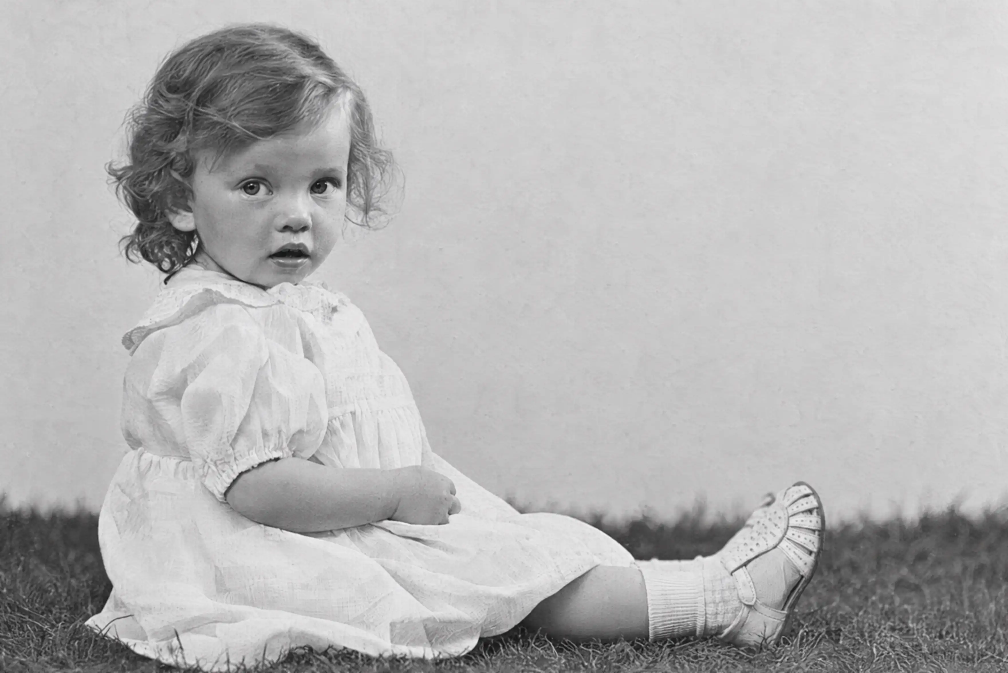 The same childhood photograph after restoration, with a clearer face, hair and dress and the large cracks removed.