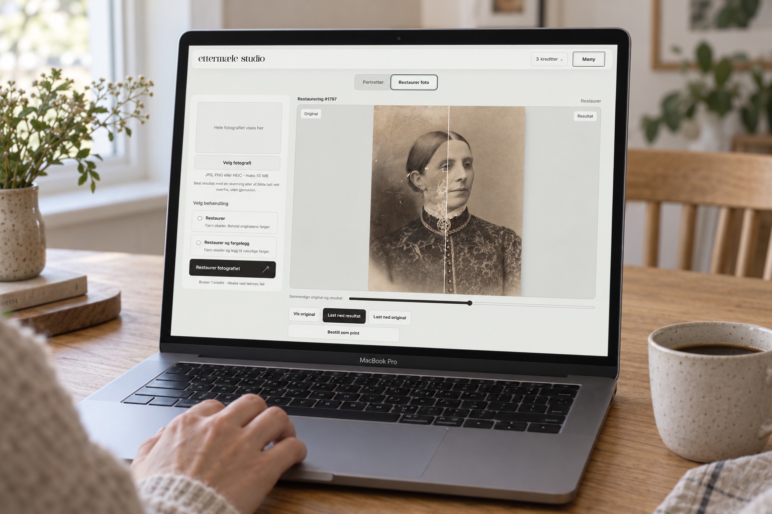 Ettermæle Studio on a MacBook Pro at a dining table. A hand rests beside the trackpad, and an old portrait of a woman is compared before and after restoration.